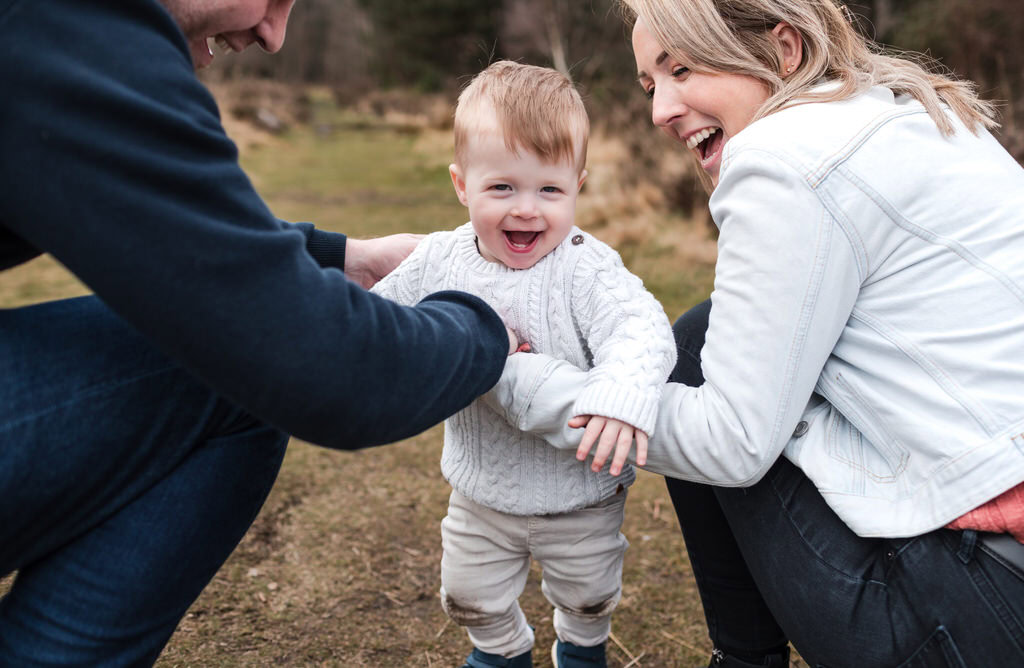 A toddler runs towards his parents during a fun family photoshoot outdoors in Birmingham