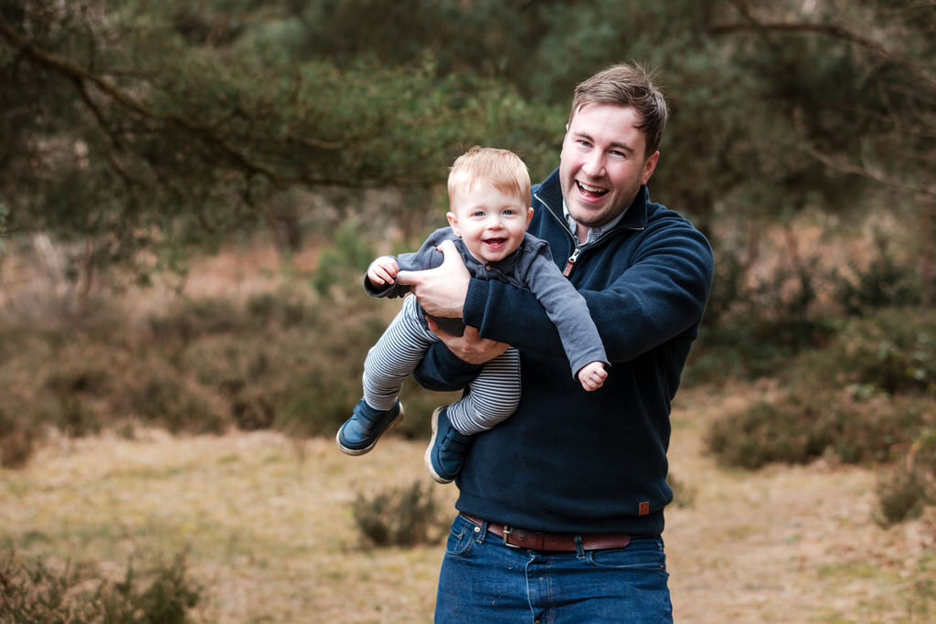 A young Dad lifts his toddler in the air during an outdoor family photoshoot in Sutton Park