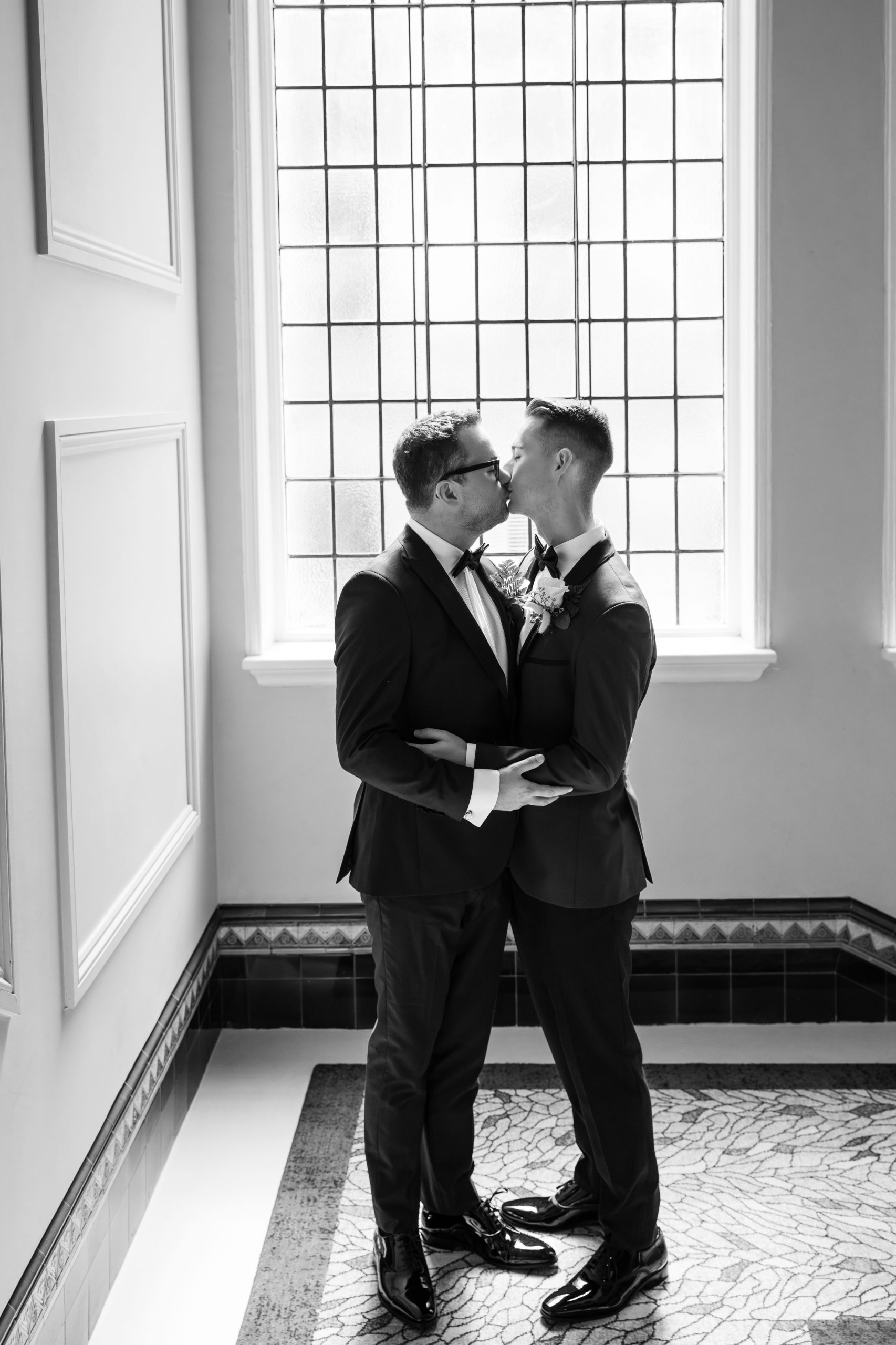 Two Grooms kiss in front of a window after their wedding taken by a Birmingham wedding photographer