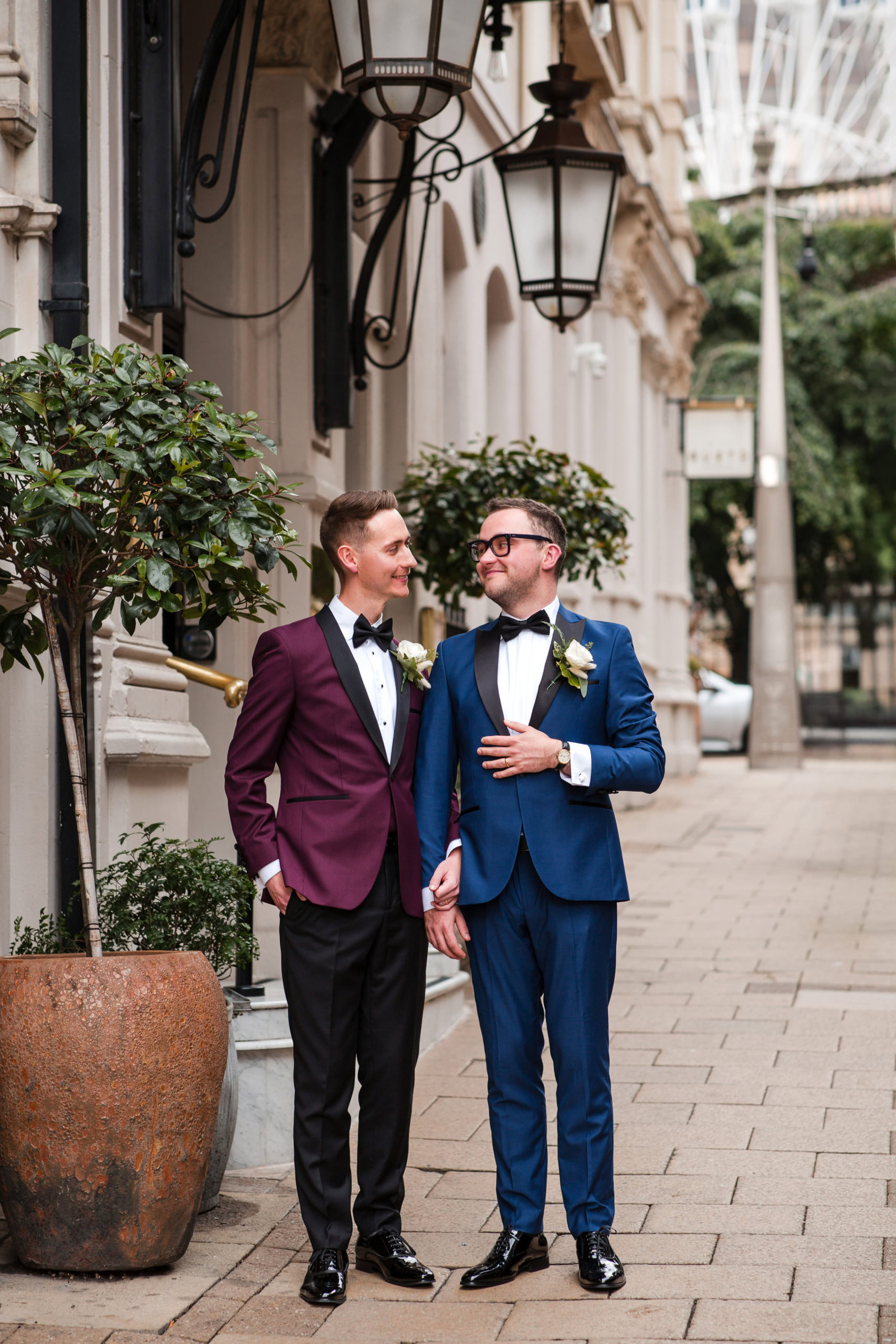 Two Grooms wearing tuxedos look at each other for wedding photos outside The Grand Hotel Birmingham