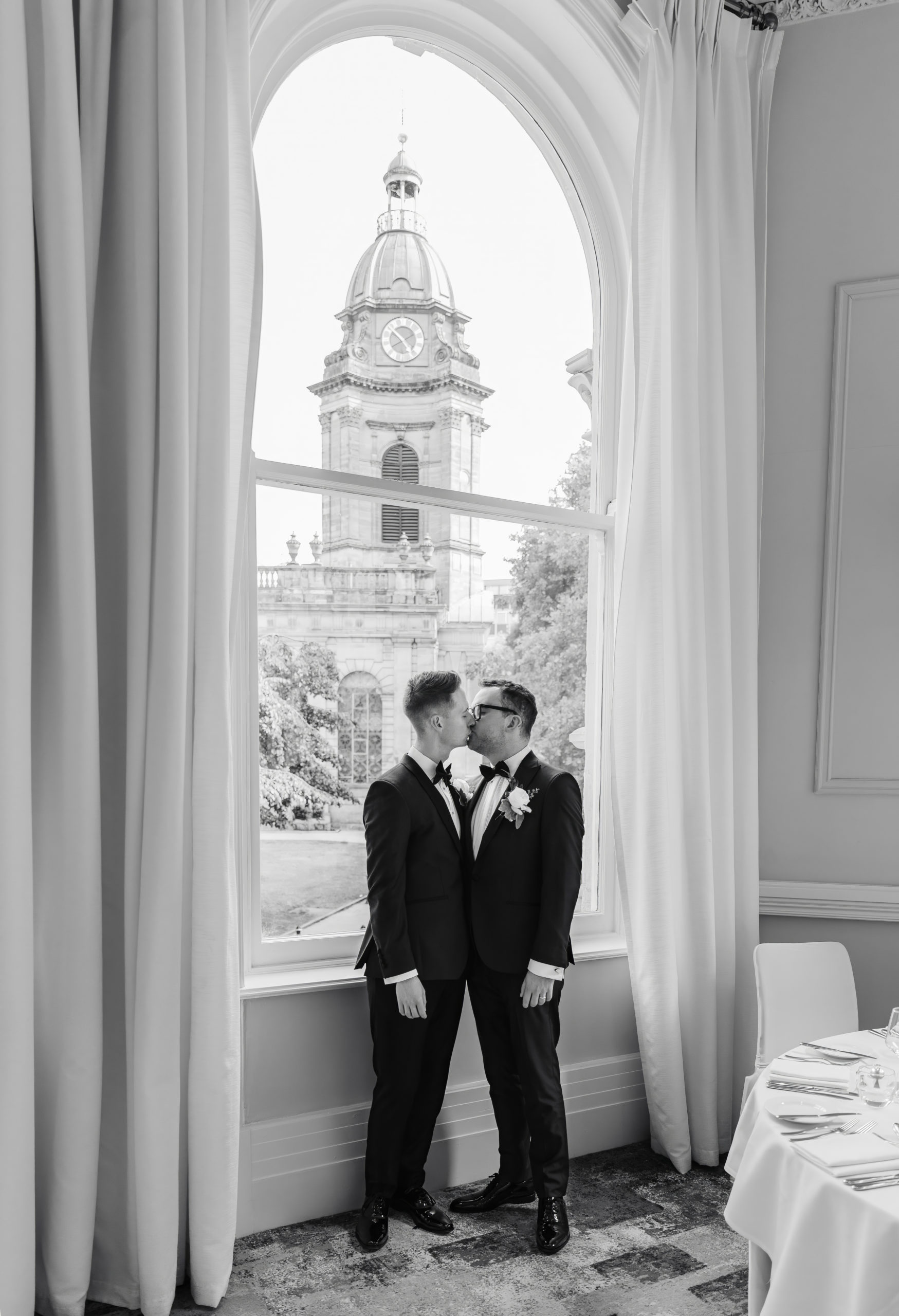 Gay couple wearing tuxedos share a kiss at their wedding venue The Grand Hotel Birmingham