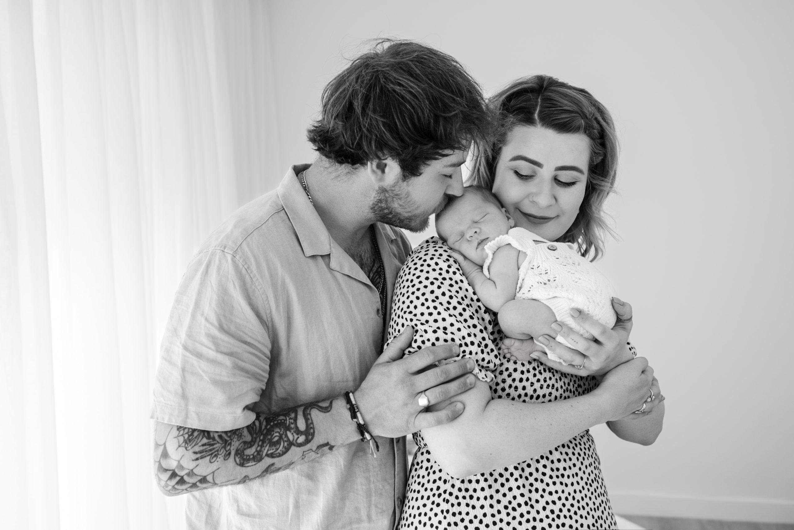 mum holding her sleeping baby on her chest while Dad kisses baby's forehead during newborn photoshoot in Birmingham studio