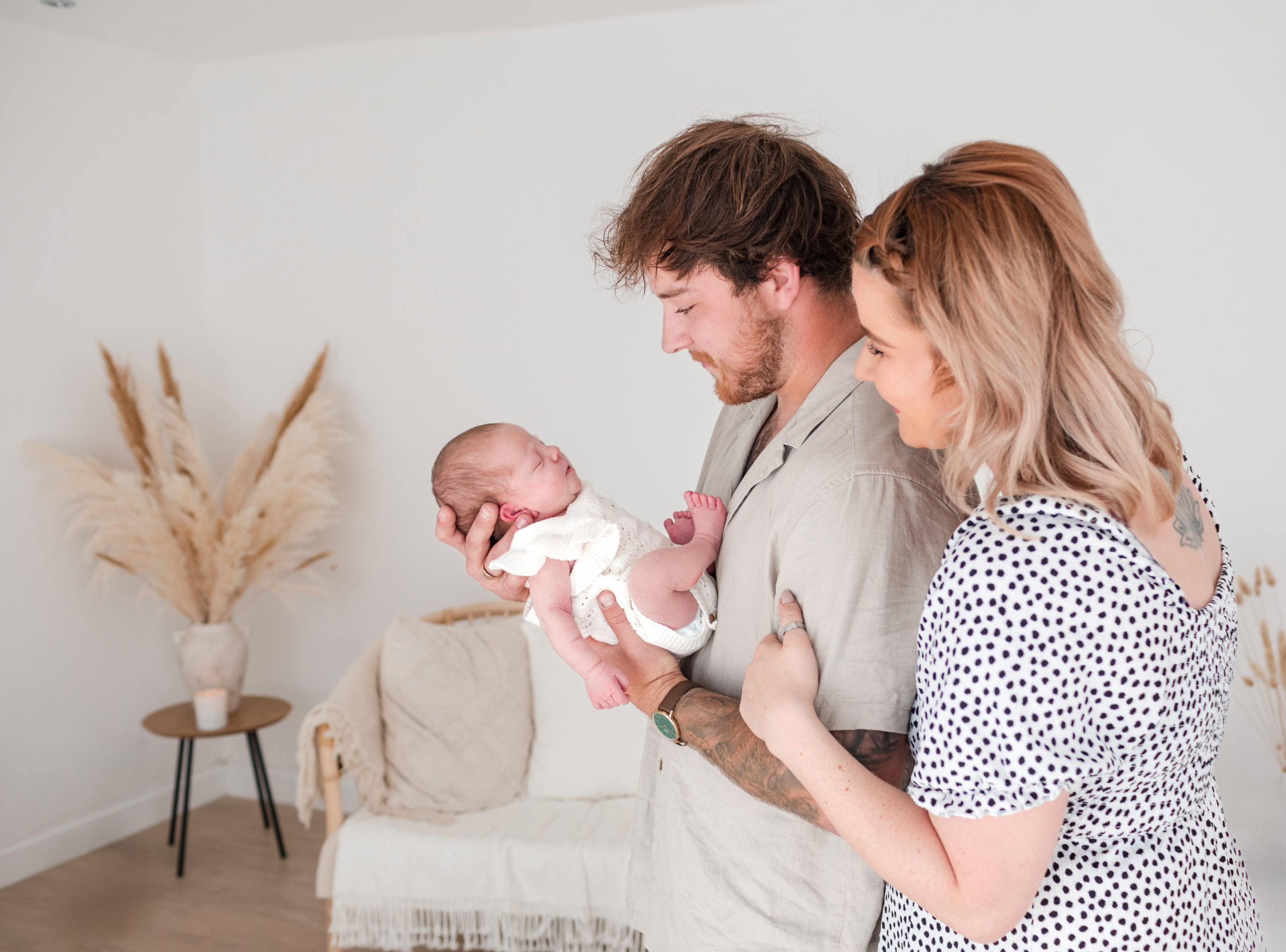 new parents hold their newborn baby in a light neutral room 