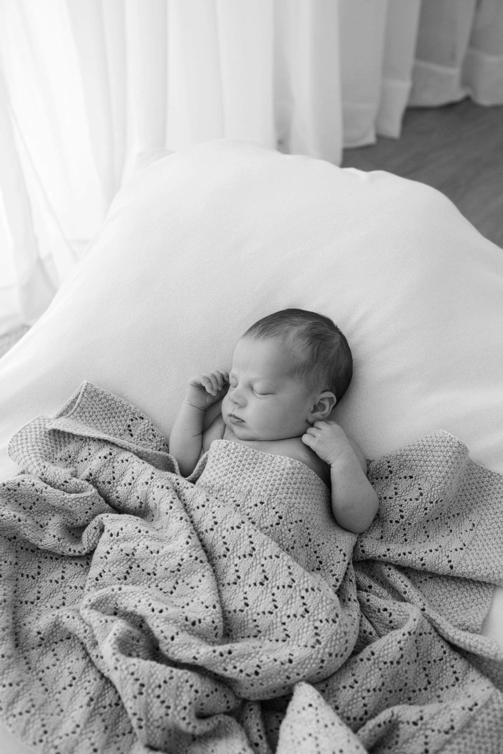 black and white photo of a newborn baby asleep lying on a posing beanbag, covered in a textured patterned blanket