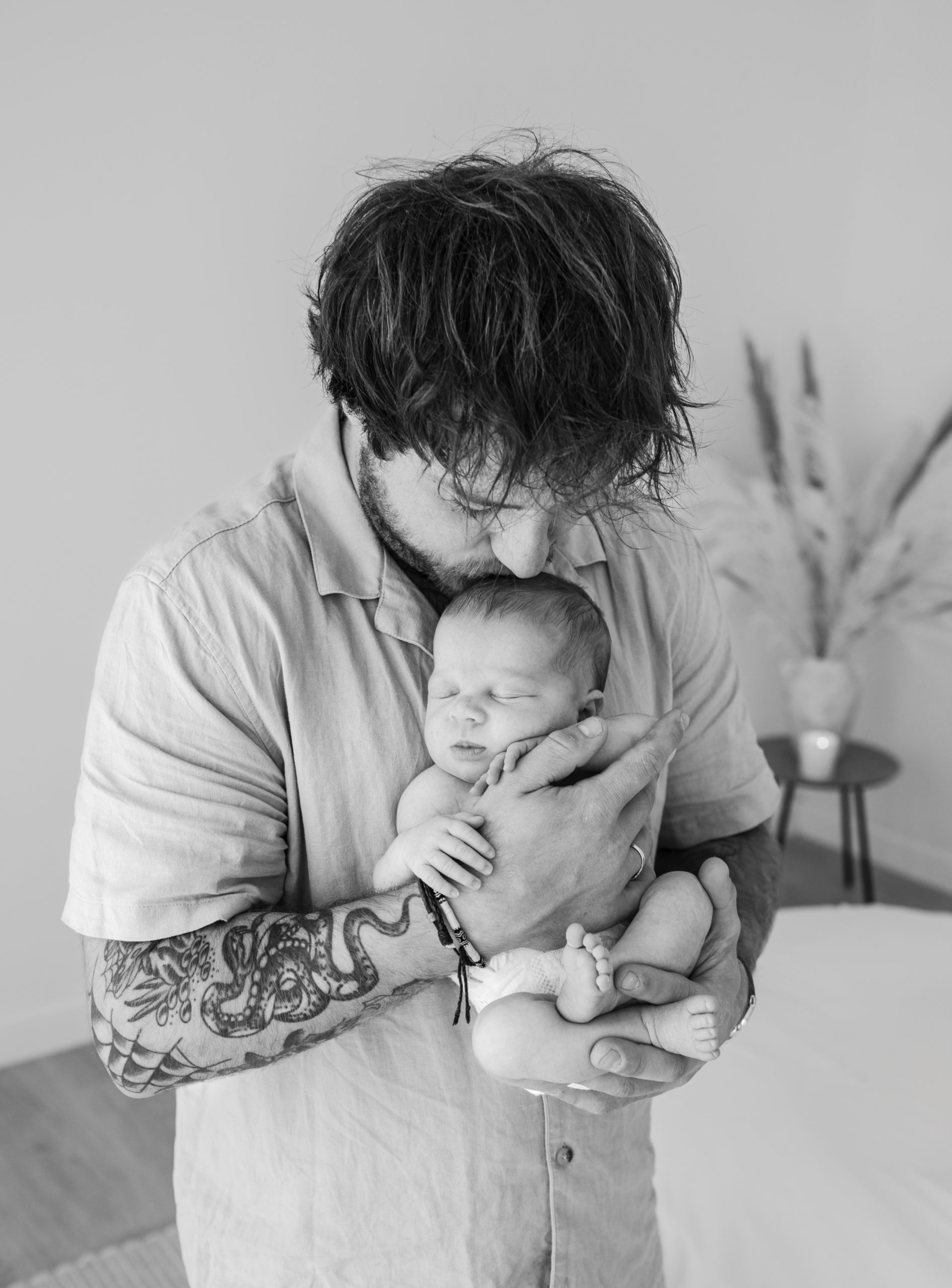 Dad with a arm tattoo cradles his newborn baby during a newborn photography photoshoot in Birmingham 
