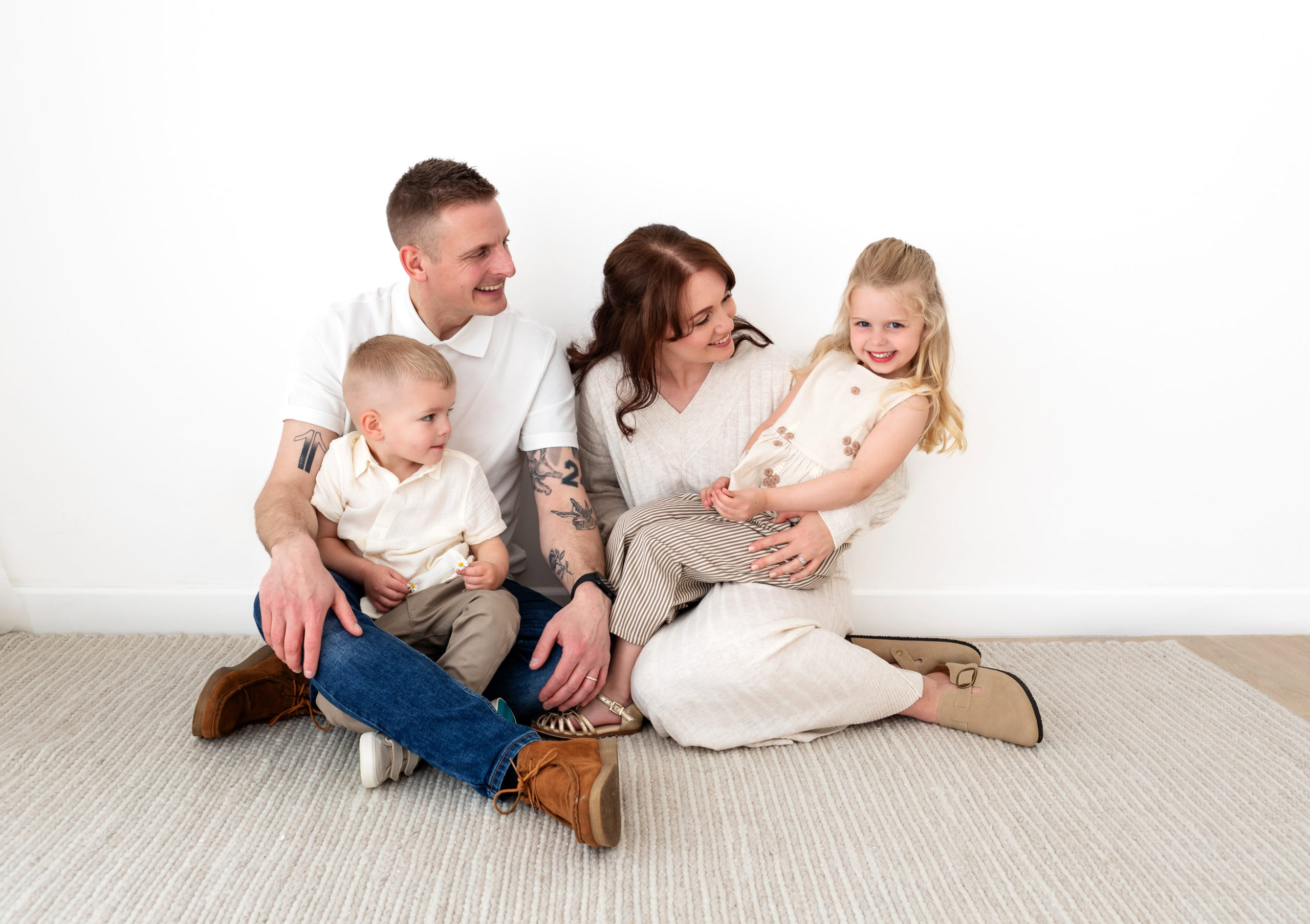 family with young children sit on a natural rug and snuggle together for a family photo