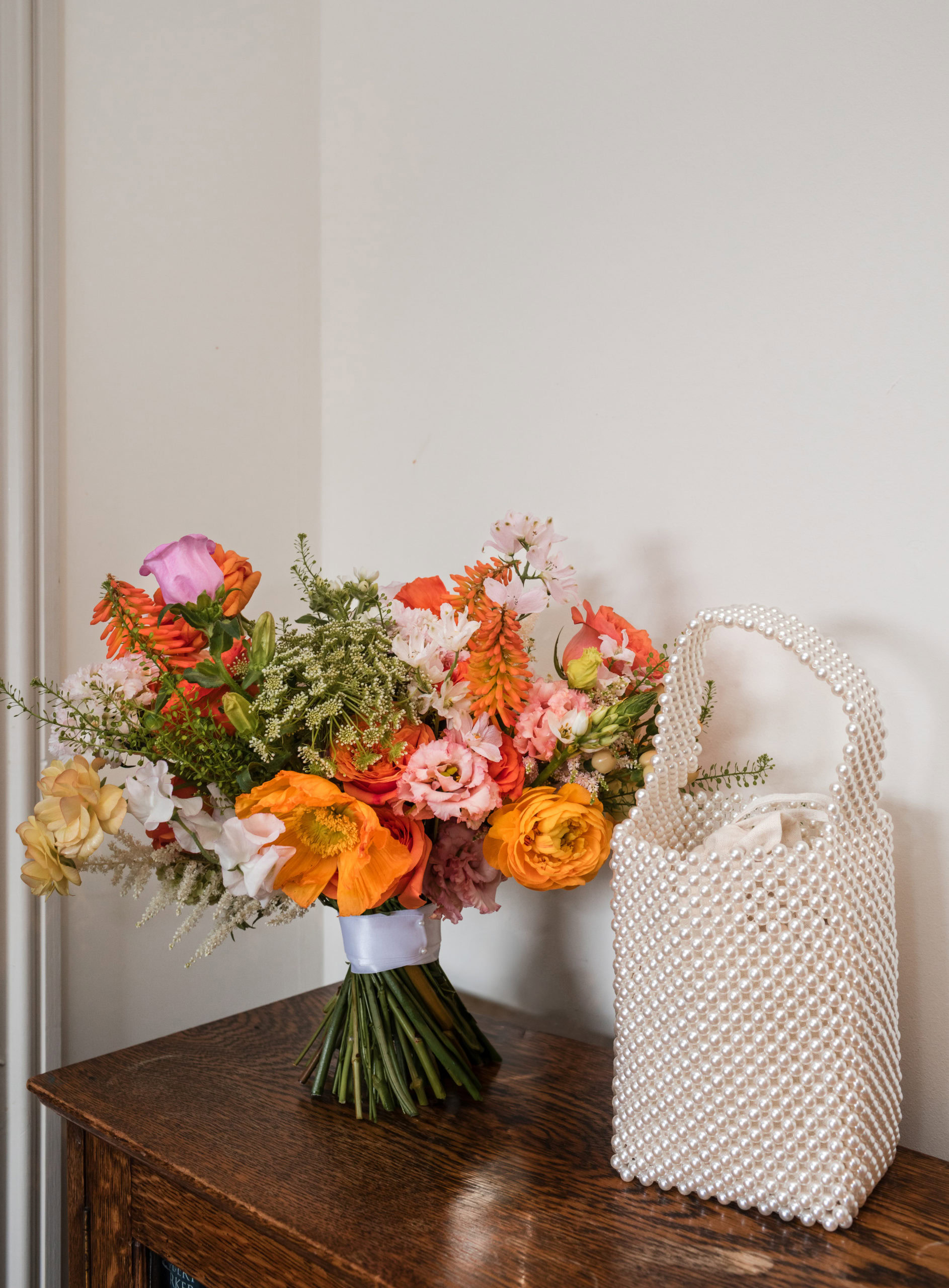 colourful orange Brides Bouquet and a pearl handbag