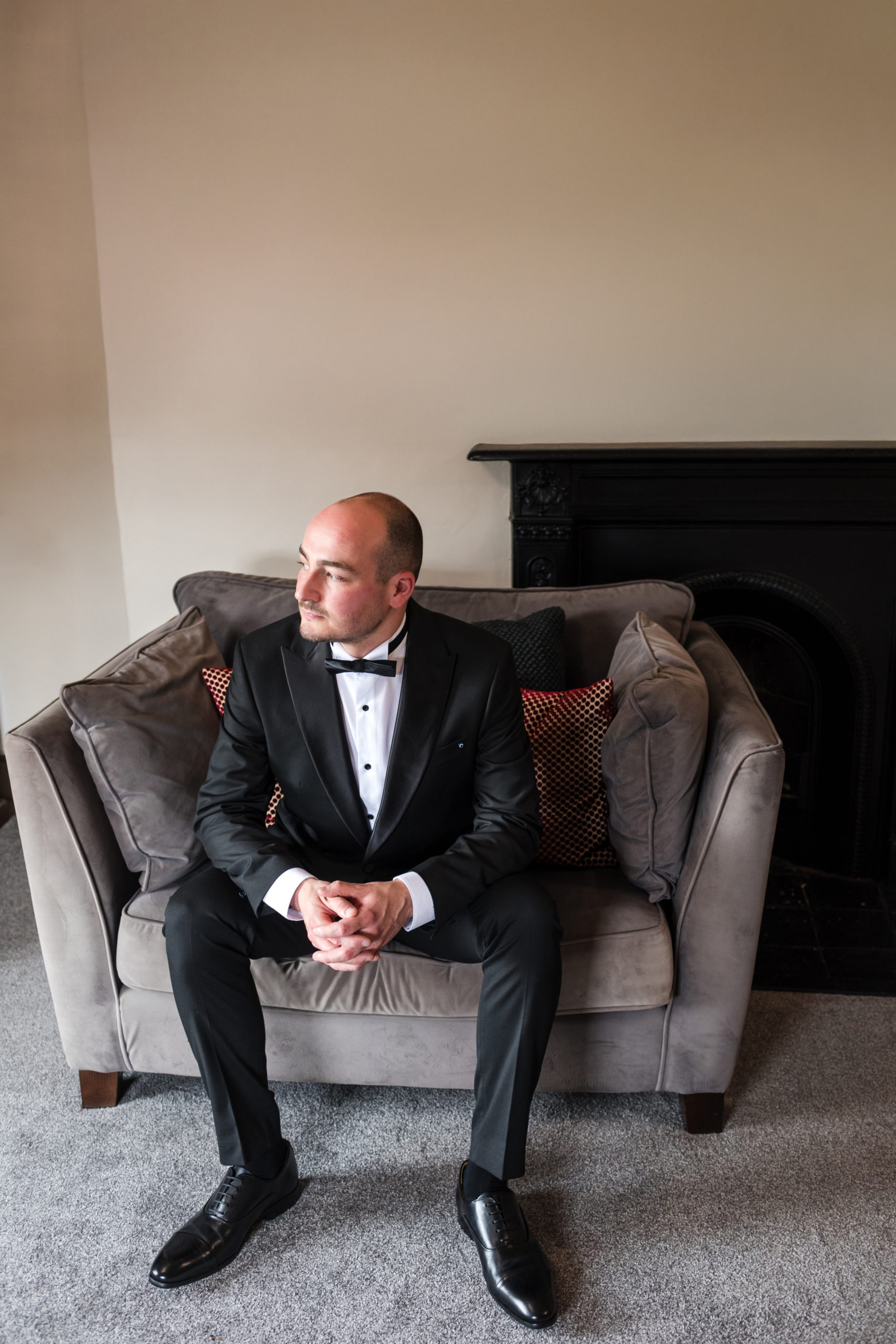 Portrait of a Groom wearing black tie sitting in an armchair before his wedding at St Johns House Lichfield