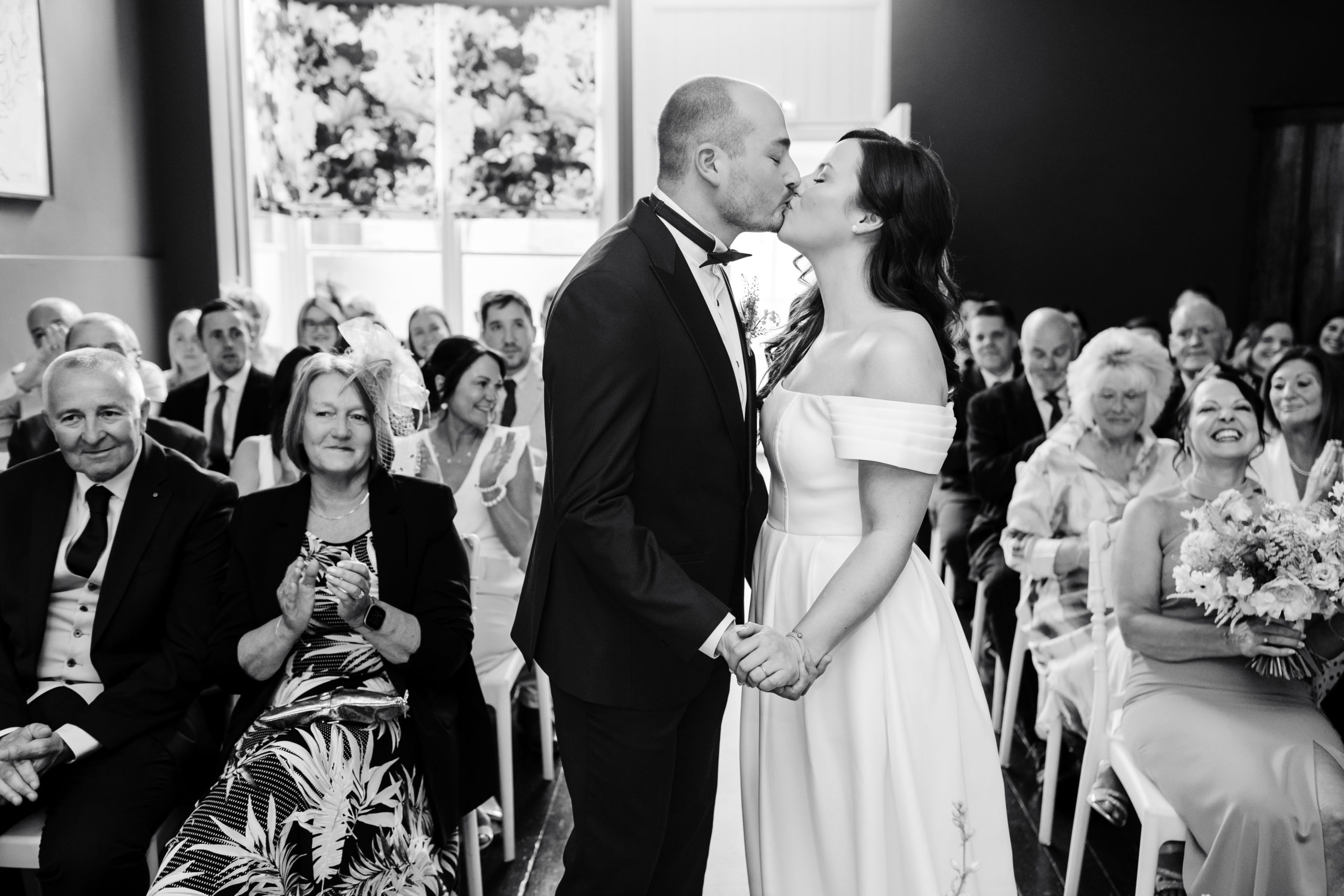 Black and white portrait of a bride and groom sharing the first kiss at their wedding ceremony in Lichfield
